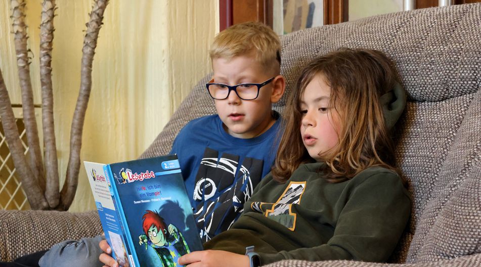 Zwei Schüler sitzen gemütlich auf einem Sessel und lesen gemeinsam in dem Buch "Hilfe, ich bin ein Vampir".