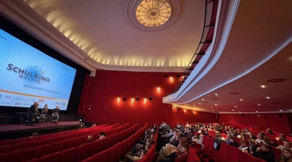 Blick in ein Kino. Vor der Leinwand findet eine Podiumsdiskussion statt, im Saal sitzen Schülerinnen und Schüler.