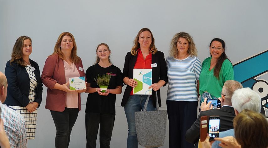 Sechs Frauen stehen bei einer Auszeichnungsveranstaltung des Berufswahl-Siegels nebeneinander und halten Urkunden, während Publikum fotografiert.