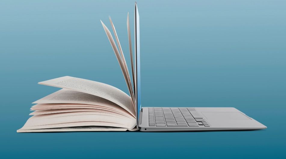 Halb geöffnetes Buch, das nahtlos in ein aufgeklapptes Laptop mit sichtbarer Tastatur übergeht.